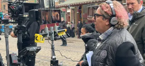 Director Tina Gharavi on the set of Night and Day wearing headphone and looking into monitors which show the actors in the scenes which are being shot