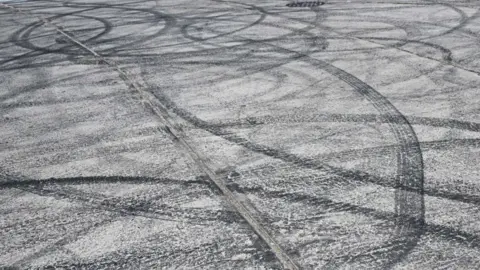Tyre marks in a car park that look as though they were made by motorists doing doughnuts.