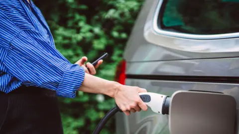 A young woman charges an electric car.