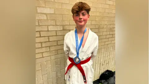 Archie smiling for the camera at a gym. He is wearing a medal.