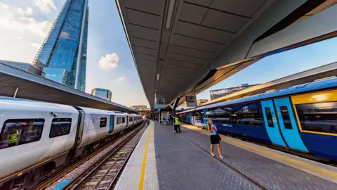 Two trains whiz through London Bridge station. A large, imposing skyscraper is seen in the distance. 