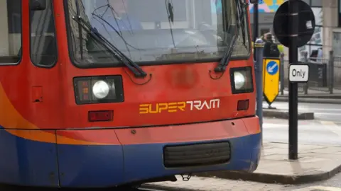 The front of a red tram. The word 'Supertram' can also be seen underneath.