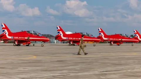 MOD The Red Arrows pictured on the tarmac at Goose Bay in Canada. A person in uniform is walking past the jets.