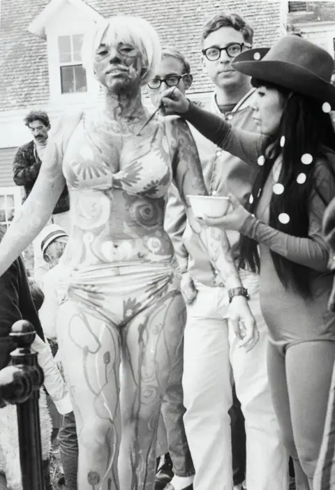 Getty Images Black & white photo of Yayoi Kusama in 1967 painting a young woman wearing a bikini at a Body Festival in Provincetown, Massachusetts.