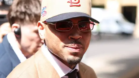 US singer Chris Brown arrives at Southwark Crown Court wearing a beige suit, glasses and a baseball cap