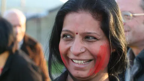 A headshot of Raxa Modha, who is looking away to her right with a smile on her face.