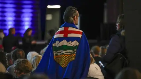 An attendee wears an Alberta flag draped around their back as they stand up during the Alberta Independence Town Hall event in Calgary, Alberta, Canada.