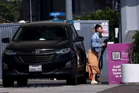 A woman fills up her black car at the petrol station
