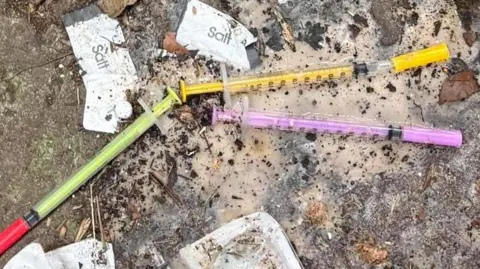 Shows three needles - green, yellow and lilac in colour on the ground. 