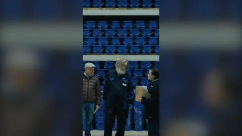 Two men and a woman stand in front of a wall full of blue buckets.
