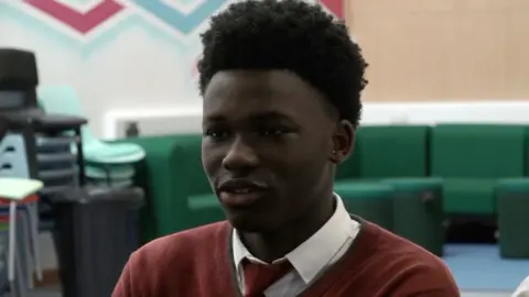 Pupil Lanre in school in a dark red school jumper and tie.