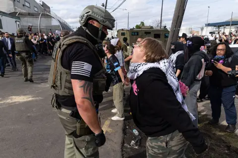 A woman shouts at an ICE agent outside the facility.