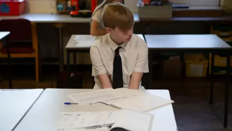 A stock image of a boy in school uniform at school in front of table with work books.