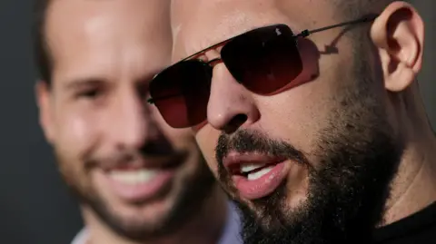 Reuters Andrew Tate, next to his brother Tristan Tate, talks to media representatives after exiting the Bucharest courthouse, in Bucharest, Romania