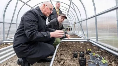 PA Media First Minister John Swinney being shown some seedlings during a visit to officially open Phoenix Future's Rae House residential rehabilitation centre in Alford, Aberdeenshire.