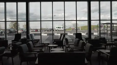 PA Media A view of what looks like a meeting lounge, with black upholstered chairs and small coffee tables, looking out through a bank of glass windows towards a car park.