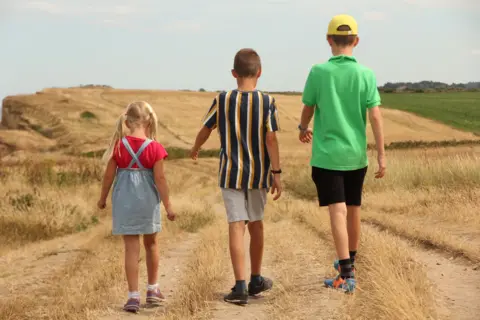 Two boys and a girl walking along a dry coastal footpath in summer wearing clothes for hot weather.
