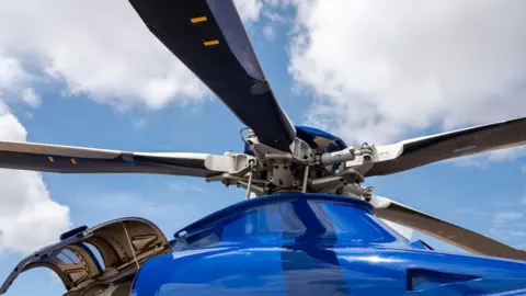A close-up view of a blue helicopter with its four blades visible against a blue sky