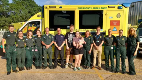 South Central Ambulance Service Sam, Emma and Sophie King are stood in front of an ambulance with the group of people involved in his treatment on the night of his cardiac arrest. 