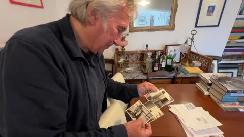 Jeff Towns at a wooden table looking at black and white photographs of Dylan Thomas at Strand Films.