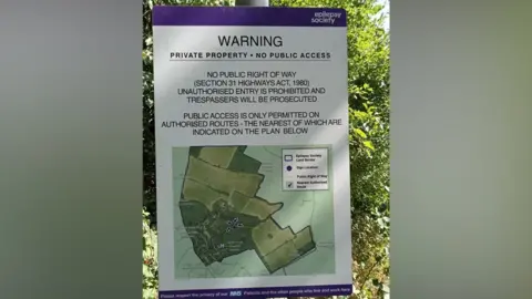 Geograph/David Hillas A warning sign mounted outdoors beside leafy greenery. It states that the land is private property with no public access and that unauthorised entry is prohibited. The sign includes a small map outlining permitted routes and borders for nearby pathways. At the bottom, there is a reminder to respect the privacy of NHS patients and others who live and work in the area.