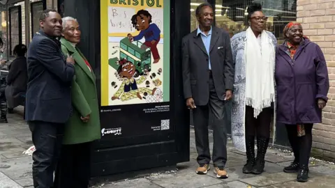 A group of pioneers from the Bristol Bus Boycott smile at the camera as they stand next to new artwork at a bus stop near The Lanes in Bristol city centre.