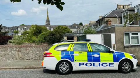 Police car in Aberdeen at scene of a drug operation in Aberdeen, a church spire is in the background.