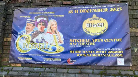 A large blue advertising banner for a Cinderella pantomime at the Mitchell Arts Centre. It has been hung on a large brick wall outside.