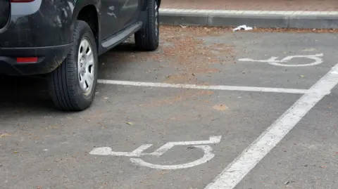 A car is parked across two disabled parking spaces