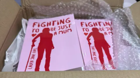 Laura Earl A box of pink books. The front cover features the silhouette of a woman using a walking stick and the text: "Fighting to just be a mum. Laura Jane Earl". The books are nestled in bubble wrap.