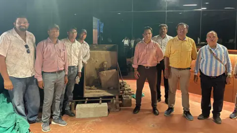 Roxy Gagdekar Chhara/BBC A photo of civil servants who are on either side of the skeleton in the museum where it will now find a house. 