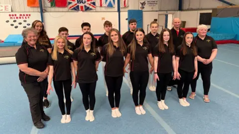 Two rows of competitors in black outfits stand on a blue gymnasium floor.