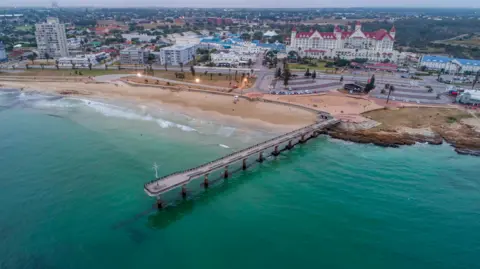 Getty Images An aerial view of Shark Rock Pier in Gqeberha. The pier can be seen jutting out from the beach over a clear ocean.
