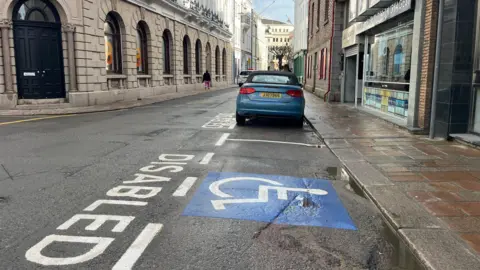 A disabled parking bay on Library Place, with a car parked in front of it.