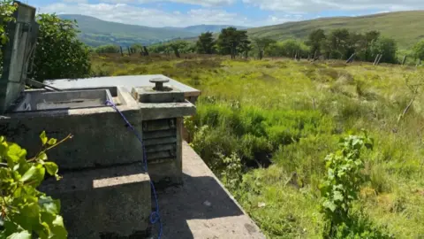 SDL Property Auctions A concrete bunker in a large green field. Rolling hills are in the background.