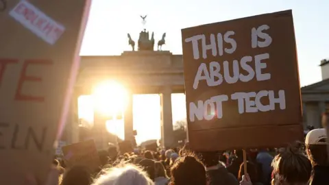 Maryam Majd/Getty Images A placard reads "This is abuse not tech" at sunset at the Brandenburg Gate in Berlin