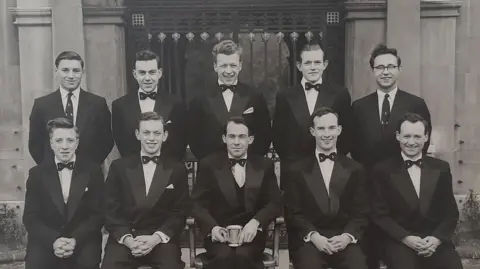 University of Cambridge A black and white photo of the Cambridge University Tiddlywinks Club in 1958. There are two rows of men, smartly dressed in suits with bow ties. Bill Steen is in the front row, second from right. Lawford Howells is in the front row on the far right and Peter Downes is on the front row, second from the left.