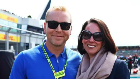 Sir Chris Hoy, wearing sunglasses and a blue top next to a woman in a dark jacket, also wearing sunglasses