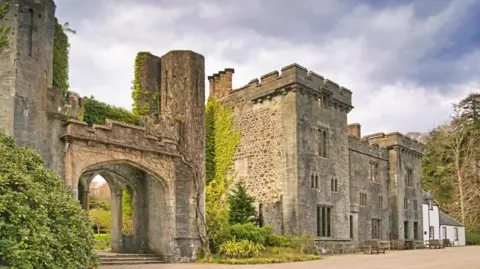 Getty Images Skye's Armadale Castle is a ruin. There is an entrance with steps and a stone arch covered in ivy and next to it a large turreted property with narrow windows.