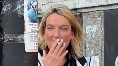Louise Gallagher, photographed leaving court. She is seen emerging from an alley and is smoking a cigarette. She has blonde shoulder-length hair.