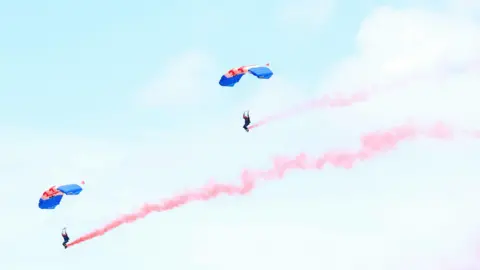 Chris Jackson/PA Wire Parachutists with red smoke devices in the sky during the Royal Cornwall Show.