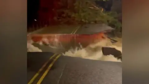 Road falls into pieces as water gushes through.