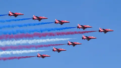 Nine Red Arrows Hawk jets flying in a V formation with red white and blue smoke