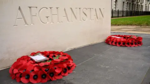 Two poppy wreaths lie in front of a stone memorial that has Afghanistan written on it.
