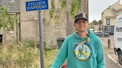 Sally Hinchcliffe in front of a sign saying cyclist's dismount