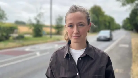 Head and shoulders image of Anna Ross. She has brunette hair tied up, is wearing a brown shirt over a white t-shirt