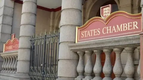 BBC Outside of the States Chamber. A large stone building with 'States Chamber' written in gold and red.