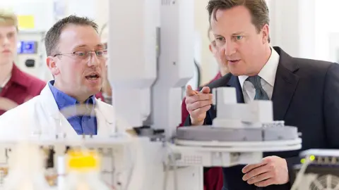 David Cameron (right) talks with analytical chemist Dave Sargeant during a visit to GlaxoSmithKline's plant at Ulverston. Mr Cameron is wearing a suit. Mr Sargeant, who has short dark hair, is wearing a white lab coat and glasses.