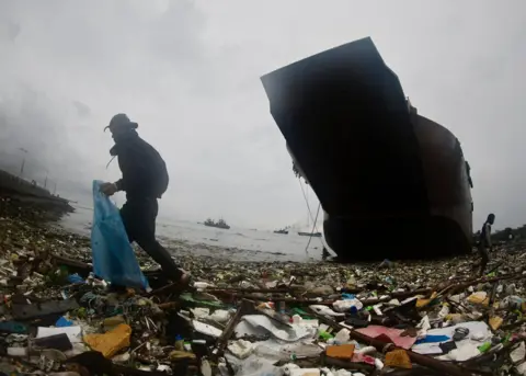 Prancis R Malasig / EPA-EFE Seorang penduduk desa mengumpulkan bahan-bahan yang dapat didaur ulang di samping sebuah kapal yang kandas di Teluk Manila, Filipina