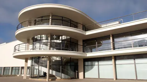 Giles Barnard/BBC The De La Warr PAvilion which faces the seafront and has three storeys, with balconies on the first and second floor. It's a cream coloured art deco style building